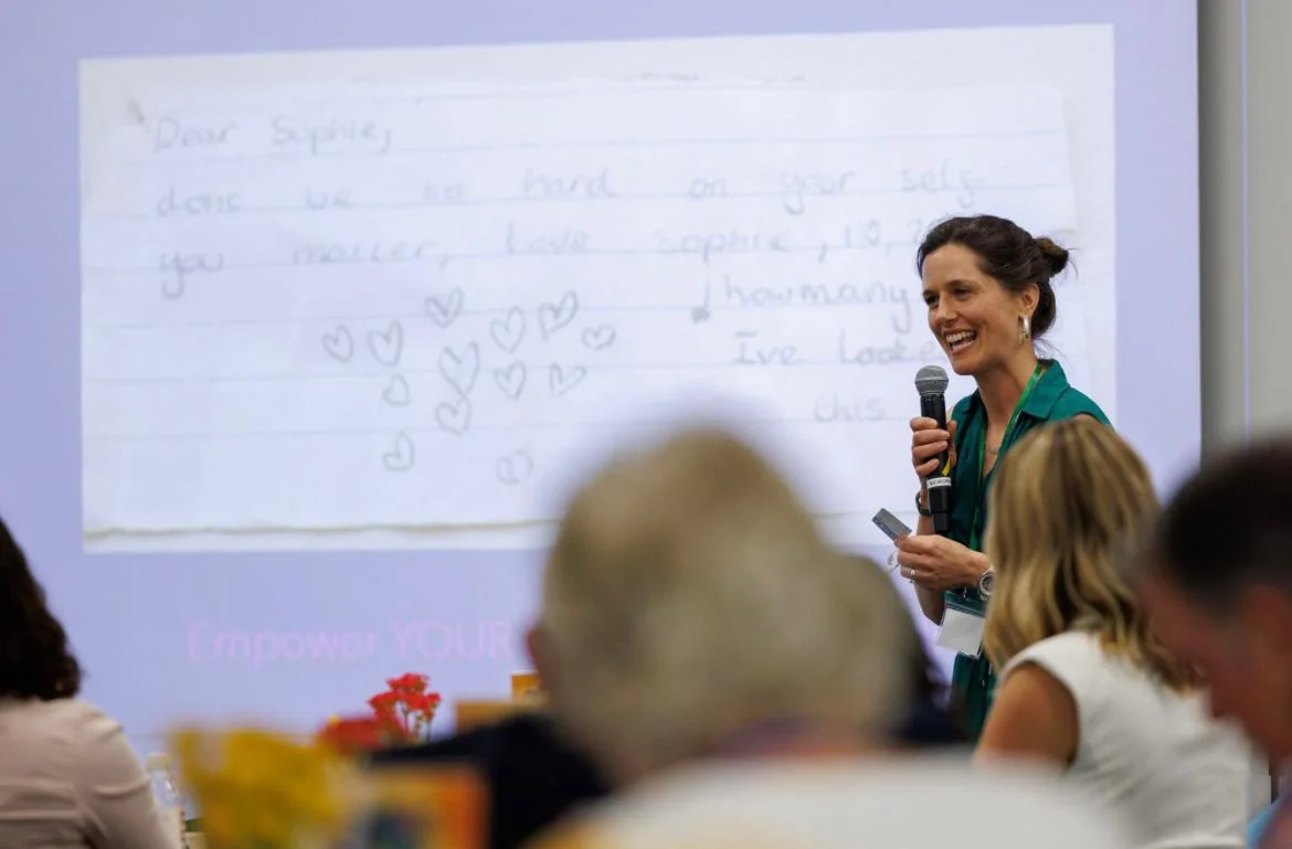 Sally speaking with a handwritten kindness message projected behind her